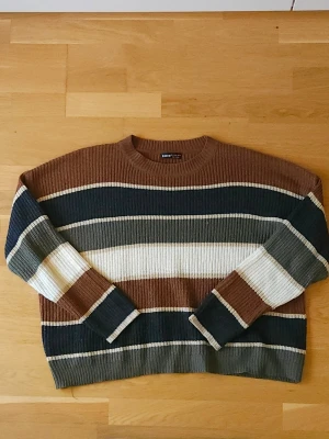 Stickad tröja  - Stickad tröja från SHEIN med breda ränder i brunt, mörkgrönt, beige, vitt och mörkblått. Tröjan har rund halsringning, lång ärm och grov ribbstickning. Perfekt för dig som gillar retrovibbar och mysiga höstlooks.