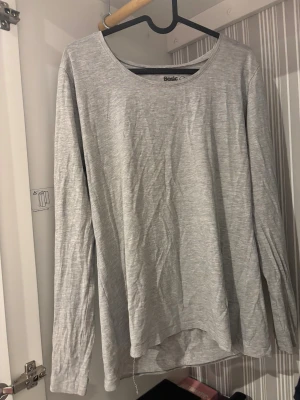 Grå långärmad topp från Basic - Säljer en enkel och stilren grå långärmad topp från Basic. Toppen har rund halsringning och är tillverkad i mjuk bomull, perfekt för en chill och avslappnad look. Passar dig som gillar minimalistisk stil och neutrala färger.