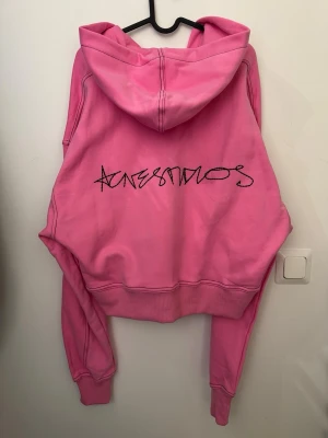 Rosa croppad hoodie från acne studios med autograph logga broderad - Rosa hoodie från acne studios med broderad logga på ryggen i form av autograf. Croppad pass form i midjan, oversized. Storlek S