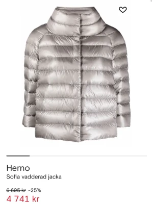 Silver pufferjacka från Herno - Säljer en snygg silverfärgad pufferjacka från Herno med hög krage och quiltad design. Jackan har en glansig finish, raka linjer och knappar framtill. Perfekt för dig som vill ha en stilren och varm jacka med cool look. 