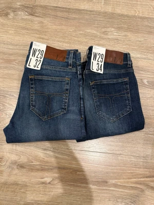 Tiger of Sweden mörkblå jeans W29 L32/L34 - Snygga mörkblå jeans från Tiger of Sweden med klassisk femficksdesign, kontrastsömmar och läderpatch bak i midjan. Jeansen har rak passform och är tillverkade i slitstarkt bomullsjeansmaterial. Perfekt för dig som gillar stilrena och tidlösa jeans.