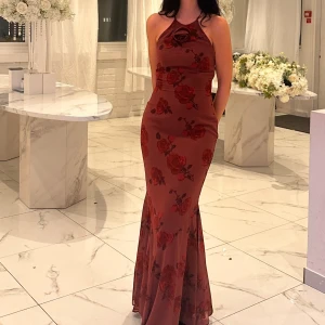 Adoore klänning  - Supersnygg vinröd långklänning från Adoore med blommigt mönster och liten rosett framtill. Jättebra skick, använd endast en gång. Jag har sytt där fram vid bröstet. Perfekt nu inför nyår och julen. Originalpris 1600kr. 