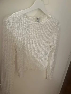 Vit spetsig långärmad blus aware - Säljer en vit långärmad blus från aware med spetsig struktur och vågig kant vid hals och ärmslut. Materialet är genombrutet och ger en luftig känsla, perfekt för dig som gillar romantisk och trendig stil.