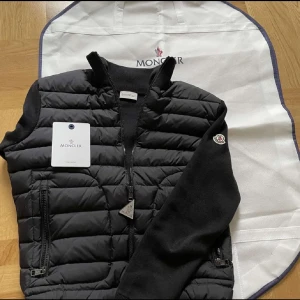 Moncler Cardigan - Nu säljs en Moncler Cardigan i fräscht skick perfekt för att hålla dig varm med stil, Storlek M. Den stora Moncler Dustbag & kort medföljer självklart. Tveka inte att skriva vid minsta fundering. 