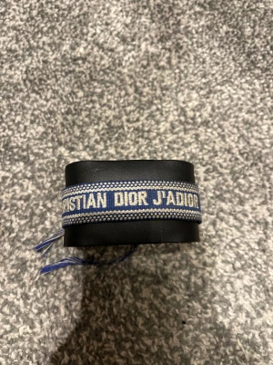Blå Christian Dior J'Adior armband - Snyggt blått armband från Christian Dior med texten 'J'Adior' broderat i beige. Armbandet är gjort i vävd bomull och har justerbar knytning med flätade snören. Perfekt accessoar för att lyfta din outfit med lite lyxig vibe. Nypris: 4459kr, mitt pris: 399kr.