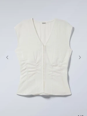 Vit korsett-topp från Weekday - Säljer en vit korsett-topp från Weekday i storlek 36. Toppen har v-ringning, är ärmlös och har snygga rynkade detaljer på sidorna. Stängs med hakar framtill och är gjord i bomullsmaterial. Perfekt för dig som gillar minimalistisk och clean stil.