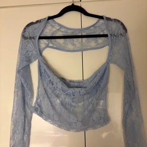 Blommig ljusblå spetstopp - Säljer en ljusblå blus från SHEIN i transparent spets med blommigt mönster. Blusen har långärmade armar, croppad passform och öppen rygg. Materialet är 100% polyester och toppen har en snygg omlott-look framtill.