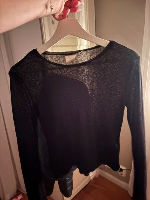 Svart mesh långärmad topp från Nelly  - Säljer en svart mesh topp från Nelly i storlek xs. Toppen är långärmad och har en tunn, transparent look som ger en cool vibe. Perfekt att styla lager på lager eller med ett snyggt linne under. Enkel rund halsringning och rak passform.