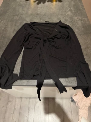 Svart omlottopp från Gina Tricot - Svart långärmad omlottopp från Gina Tricot med knyt framtill. Tunn och mjuk i materialet, perfekt för lager på lager. Djup v-ringning och smal passform som framhäver siluetten.💞💞