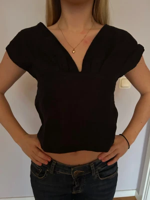 Svart croppad blus med v-ringning - En svart topp i linnetyg med v-ringning fram och öppen rygg. 💕