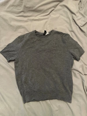 Snygg grå topp  - Snygg grå stickad topp med korta ärmar och rund hals. Perfekt för dig som gillar enkel och stilren design. Ribbad kant vid hals, ärmslut och nederkant ger en schysst detalj. Passar till både jeans och kjol för en chill look. 