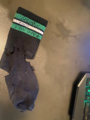 Signerad ninja low taper fade strumpa  - Cool svart strumpa med gröna och vita ränder upptill, ribbad design och texten 'Lowtaper' signerat från the massiva man himself, ninja. Strumpan har en klassisk form och är tillverkad i mjukt bomullsmaterial. Perfekt för dig som gillar streetwear och vill sticka ut med en unik detalj. 