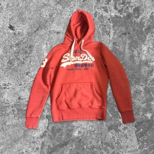 Röd Superdry hoodie med tryck - Snygg röd hoodie från Superdry med stort vitt tryck på bröstet och siffran 23 på ärmen. Tröjan har huva med vita snören och en klassisk magficka. storlek S/M, Kom gärna med frågor🤝