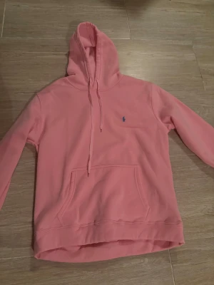 Rosa hoodie från Polo Ralph Lauren XL - Snygg rosa hoodie från Polo Ralph Lauren i storlek XL. Tröjan har huva med snörning, klassisk känguruficka och det ikoniska blå Polo-logot på bröstet. Mjuk insida i fleece och långärmad modell, perfekt för chill dagar.