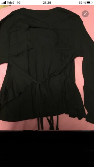 Svart långärmad topp med öppen rygg och knyt - Svart långärmad topp med rund hals och snygga knytband i midjan. Baksidan har en öppen rygg med band som kan knytas för en cool detalj. Materialet känns mjukt och lätt, perfekt för dig som gillar stilrena plagg med twist.