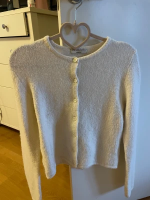 Vit kofta från Gina Tricot XS - Mysig vit kofta från Gina Tricot i storlek XS. Koftan har rund hals, långa ärmar och knäpps med vita knappar framtill. Materialet är fluffigt och stickat, perfekt för att hålla värmen under kyliga dagar. Enkel och stilren design som funkar till många outfits.