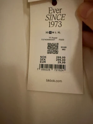 Vit asymmetrisk topp från Bik Bok - Säljer en vit, stilren topp från Bik Bok i storlek S. Toppen har en cool asymmetrisk form med draperad framsida och är ärmlös. Materialet känns mjukt och har en lätt glans, perfekt för dig som gillar minimalistisk och modern stil. Dragkedja i ryggen för enkel påklädning.