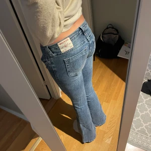 True Religion blå/rosa bootcut - Helt nya! Aldrig använda! Ultra low rise! Snygga blå jeans från True Religion med ikoniska bakfickor och kontrastsömmar. Modellen är bootcut och har en klassisk femficksdesign samt patch med logga bak i midjan i ljusrosa. Perfekt för dig som gillar en bekväm passform och coola detaljer.