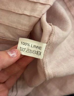 Ljusrosa linneskjorta från Budrys Design - Snygg ljusrosa skjorta från Budrys Design i 100% linne. Skjortan har klassisk krage, knappar framtill och trekvartsärmar med knappdetalj vid ärmslutet. Luftig och stilren modell som passar perfekt till varmare dagar.