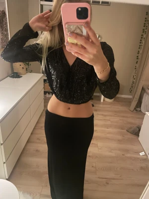 Svart glittrig topp - Säljer en svart glittrig croppad topp från H&M med paljetter. Toppen har lång ärm, v-ringad framtill och resår i midjan. 