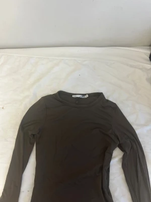 Brun långärmad topp från Lager 157 HELT NY!! - Slimmad brun långärmad topp från Lager 157 med rund halsringning. Materialet är mjukt och stretchigt, perfekt för lager-på-lager eller att bära som den är. Enkel och stilren design utan mönster eller detaljer, passar dig som gillar minimalistiskt.