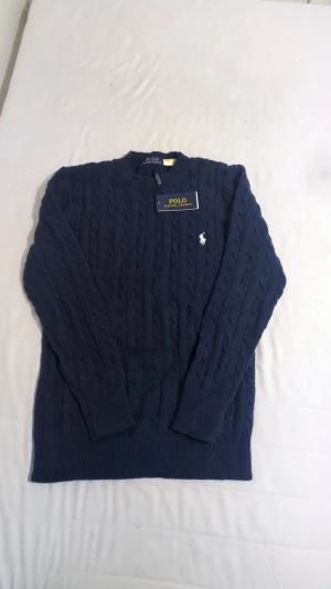 Mörkblå stickad tröja Polo Ralph Lauren - Snygg mörkblå stickad tröja från Polo Ralph Lauren med klassiskt kabelstickat mönster och broderad vit logga på bröstet. Rund hals och långa ärmar, perfekt för dig som gillar stilrena och tidlösa plagg. Taggen sitter kvar.