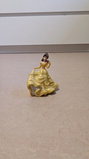  Belle från skönheten och Odjuret , Disney figur  - Disney figur, Belle från Skönheten och Odjuret. Belle har på sig en klänning. Klänningen har en lång, böljande kjol med glittriga detaljer och offshoulder-ärmar. Perfekt för dig som älskar sagolika och pampiga Disney figurer. Mycket bra skick har endast använts som dekoration 