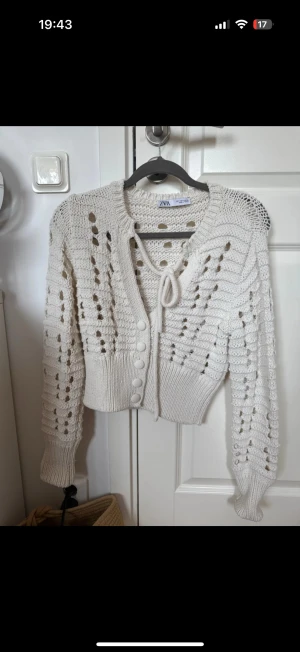 Vit stickad kofta från Zara - Supersöt vit stickad kofta från Zara med hålmönster, knytband vid halsen och stora knappar framtill. 