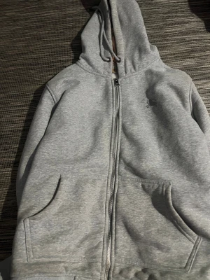Grå Burberry hoodie med rutig huva - Snygg grå hoodie från Burberry med dragkedja och klassisk rutig insida i huvan. Tröjan har broderad logga på bröstet, snörning i huvan och två fickor framtill. Perfekt för dig som gillar stilrena detaljer och ikoniskt mönster. Sår storlek xl men är Mellan M och L, passar båda bra