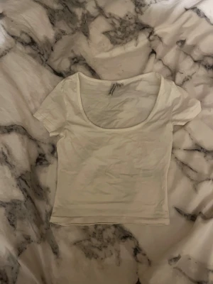 Vit croppad topp från H&M Divided - Säljer en vit croppad topp från H&M Divided i storlek XXS. Toppen har rundad, djup urringning och korta ärmar. Enkel och clean design som funkar till många olika stilar. Materialet är mjuk bomull som känns skönt mot huden.