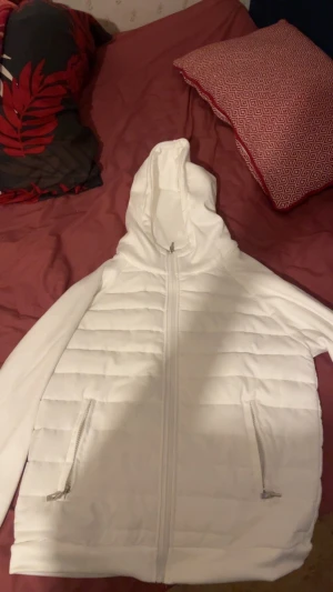 Vit quiltad pufferjacka med huva - Säljer en vit pufferjacka från H&M med quiltade paneler och huva. Jackan har två fickor med dragkedja och hel dragkedja framtill. Perfekt för dig som gillar stilren och enkel design. Passar dig som vill ha en jacka med lite volym och skön känsla.
