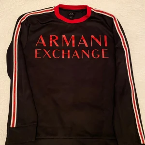  Armani Exchange tröja S - Snygg svart tröja från Armani Exchange med röd text på framsidan. Tröjan har långa ärmar med röd och vit randig detalj längs ärmarna och en röd krage.