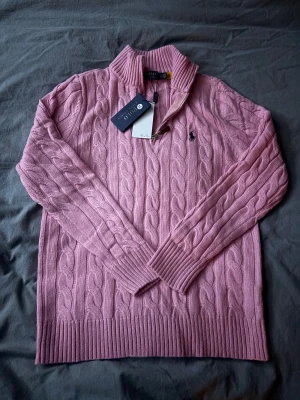 Rosa stickad tröja Polo Ralph Lauren - Säljer en rosa stickad tröja från Polo Ralph Lauren i storlek M. Tröjan har kabelstickat mönster, half zip-dragkedja och ribbad krage. Klassisk logga broderad på bröstet. Perfekt för dig som gillar preppy stil och vill ha något snyggt och bekvämt.