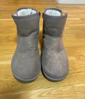 Vattentäta Grå vinterskor - Mysiga boots i grå mocka med rund tå och platt sula. Skorna har ett fluffigt vitt foder på insidan som gör dem perfekta för kyliga dagar. Enkla att dra på och av, stilrena och passar till det mesta. Perfekta för dig som vill ha både stil och komfort.Varmfodrade boots från skopunkten Vox märke i fin beige farg. Stl 39