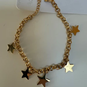 Guldigt armband med stjärnhängen - Armband i guldtonad stål med fem stjärnformade hängen, varav en är dekorerad med små glittrande stenar. Kedjan är grov och ger ett trendigt uttryck. Perfekt för dig som vill sticka ut med coola detaljer och stjärnglans.