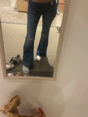 Blå väldigt lågmidjade bootcut jeans med slitningar - Säljer ett par blå bootcut jeans med snygga slitningar på knäna och låret. Jeansen har låg midja och klassiska fickor både fram och bak. Endast provade och dom säljs inte längre därav priset❤️från Gina tricot teen i storlek xs och dom sitter som en xs ockå❤️skriv för mer frågor!!!! 