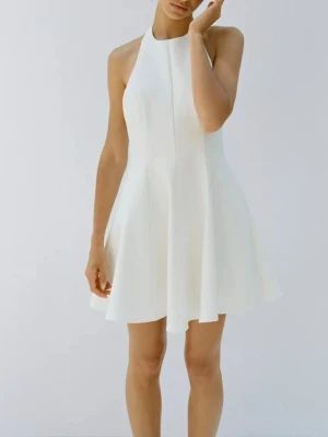 Vit halterneck kortklänning - Supersnygg vit kortklänning med halterneck och öppen rygg. Klänningen har en A-linjeformad siluett och stängs med knappar i nacken samt dragkedja bak. 