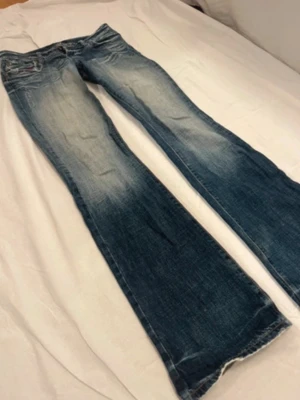 Blå bootcut jeans  - Snygga blå bootcut jeans med slitna detaljer och ljus tvätt. Klassisk femficksmodell med kontrastsömmar och coolt märke på bakfickan. Jeansen har låg midja och är tillverkade i jeansmaterial och köpa på Plick men tyvärr alldeles för stora för mig. Fickorna har ett hål i sig men tror det är en del av designen och sedan är de avklippta längst nere. Skulle säga storlek M. Skriv för frågor ❣️