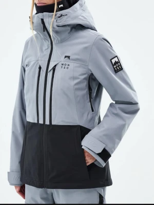 Gråblå och svart vindjacka från Montec - Snygg vindjacka från Montec i gråblå och svart med huva och flera dragkedjor framtill. Jackan har logotyp på bröstet och ärmen, samt justerbara muddar med kardborre. Perfekt för dig som gillar outdoor och vill ha en stilren look.