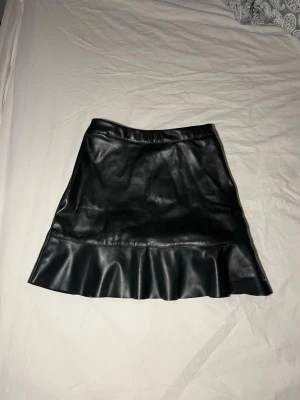 Svart kort kjol med volang från Kappahl - Säljer en svart kort kjol från Kappahl i skinnimitation med snygg volang längst ner. Kjolen har en enkel och stilren design som ger en cool vibe. Perfekt att matcha med en stickad tröja eller t-shirt för en snygg outfit! Pris kan ALLTID diskuteras och jag tar gärna emot prisförslag! Kjolen är för liten för mig så säljer den därförrrr💕