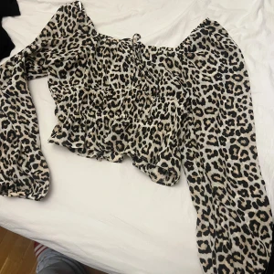 Leopardmönstrad blus från H&M - Säljer en snygg leopardmönstrad blus från H&M med offshoulder och långa, vida ärmar. Toppen är croppad och har volangdetaljer som ger en cool och trendig look. Perfekt för dig som vill sticka ut med ett djurmönster!