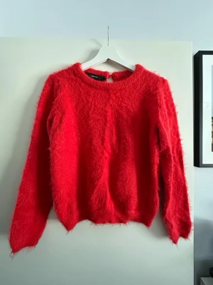 Röd fluffig stickad tröja - Supermjuk och fluffig röd stickad tröja från Vero Moda. Rund halsringning och långärmad modell . Baksidan har en öppning upptill som ger en snygg tusch. 