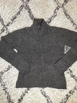 Grå stickad kofta från Columbia - Mysig gråmelerad stickad kofta från Columbia med dragkedja hela vägen och hög krage. Perfekt för kyliga dagar och enkel att matcha med allt. Klassisk passform och diskret logga på bröstet.