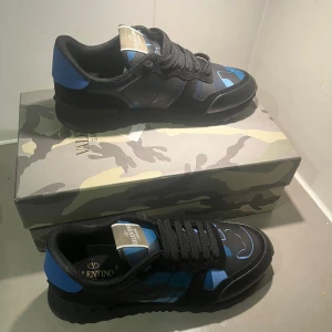 Valentino Garavani Rockrunner sneakers stl 43-42 - Snygga Valentino Garavani Rockrunner sneakers med svart och blått kamouflagemönster. Skorna har platt sula, rund tå och snörning. Materialmix av skinn och mocka med coola detaljer. Kommer med originalkartong och dustbag.