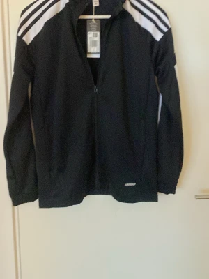 Träningskofta - En svart träningskofta, från Adidas, i storlek 164. Helt oanvänd och i mycket bra skick.