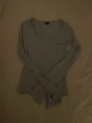 Ljusblå långärmad topp - Säljer en enkel och stilren ljusblå långärmad topp med rundad urringning. Perfekt att matcha med jeans eller kjol för en clean look. Materialet känns mjukt och stretchigt, vilket gör den bekväm att bära hela dagen.