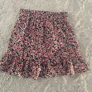 Blommig volangkjol från Uniq Young - Supersöt kort kjol från Uniq Young med blommigt mönster i rosa, svart och vitt. Kjolen har bred resår i midjan och volang längst ner för extra flowy känsla. Perfekt för dig som gillar färg och mönster!