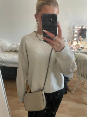 Beige axelväska med kedja  - Snygg beige axelväska med mörk silverfärgad kedja som axelrem och coola nitar längs kanterna. Kedjan är lång så passar nog en vuxen, men jag som tonåring satt ett hårband med en knut vid axeln då passa den super, tips! Aldrig använt, inga tecken på användning eller rost💓