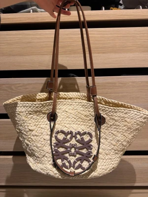 Loewe beige shoppingväska i flätad halm - Säljer en ikonisk shoppingväska  i flätad halm med bruna handtag och den klassiska Loewe-loggan i brunt skinn framtill. Perfekt storlek för att bära allt du behöver och ger en chill sommarkänsla. Använd ett fåtal gånger. Skriv innan du köper 