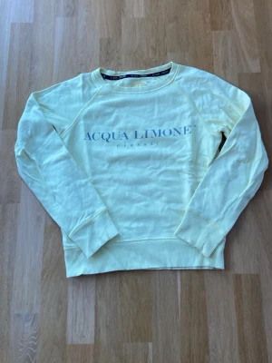 Gul sweatshirt från Acqua Limone - Fräsch ljusgul sweatshirt från Acqua Limone med tryckt logga framtill. Tröjan har rund hals, långa ärmar och ribbade muddar vid ärmslut och nederkant. 